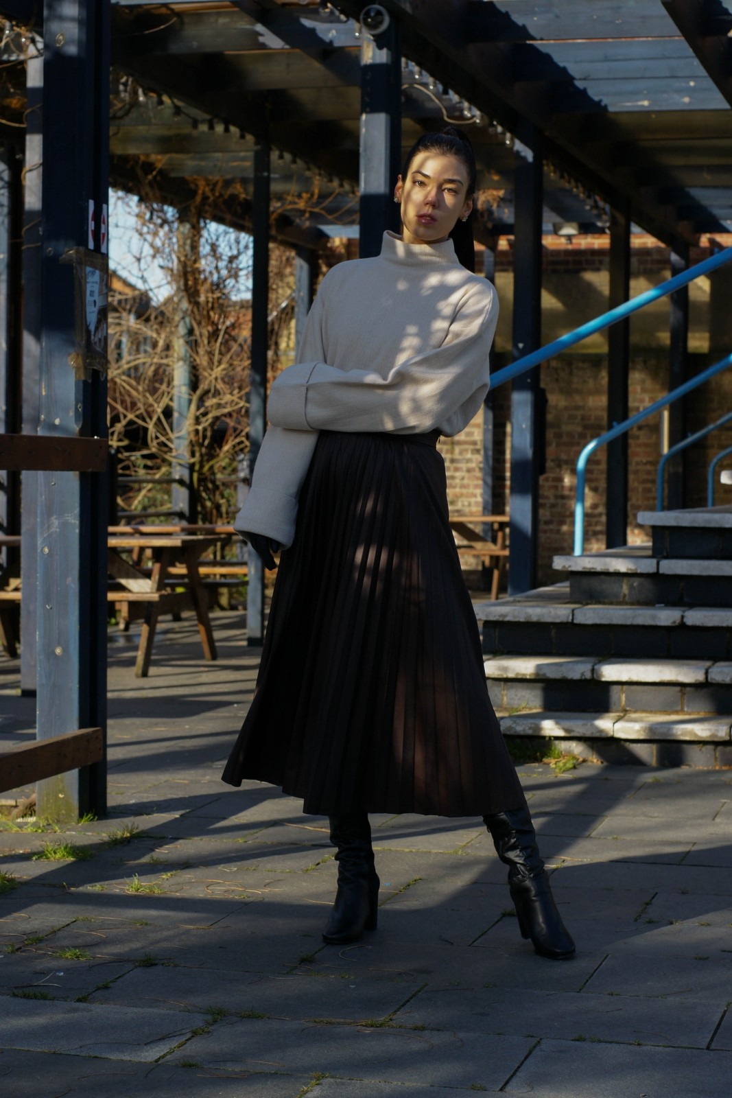 Brunette girl wearing leather pleated skirt, white jumper and leather boots